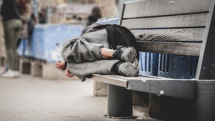 Senior man homeless wearing sweater and cloth gloves with sitting on cardboard and tying laces on shoes. Close up of asian man homeless in shelter and wear leather shoes boot and tie lace his shoes.