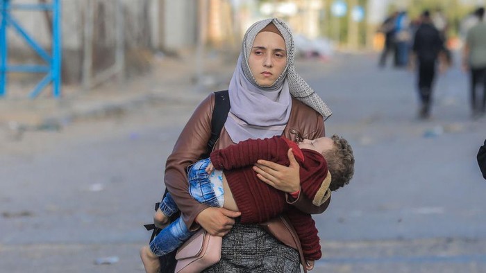 18 November 2023, Palestinian Territories, Gaza City: A woman carries a baby as Palestinian families flee Gaza City and other parts of northern Gaza towards the southern areas amid ongoing battles between Israel and the Palestinian Hamas Group.. Photo: Mohammed Talatene/dpa (Photo by Mohammed Talatene/picture alliance via Getty Images)