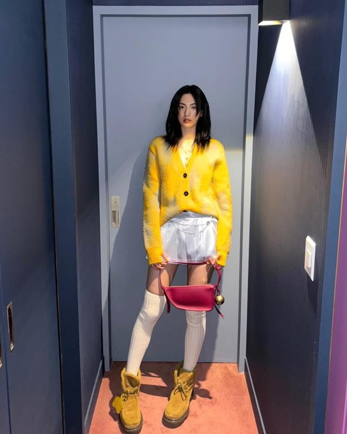 Nana terlihat mempesona dalam pilihan gaya vintage-nya dengan kardigan berwarna kuning cerah. Ia memadukannya dengan rok mini lipit berbahan satin, dan mengenakan kaos kaki selutut untuk memberikan kesan hip school look./ Foto: Elle.co.kr