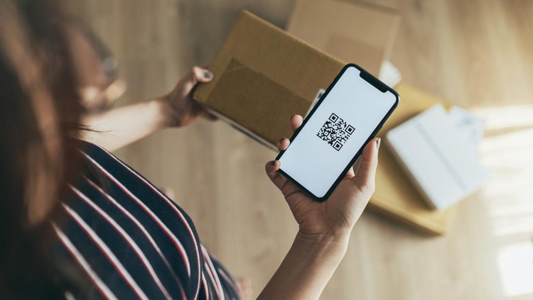 young Asian woman checking smartphone while receiving a parcel at home