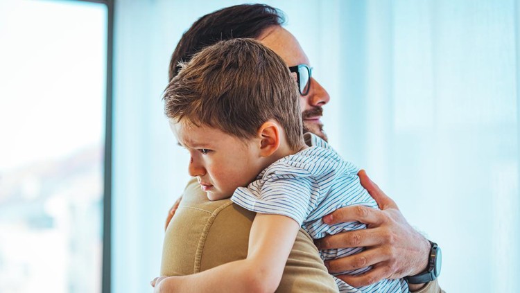 Portrait of a crying child on hands a father. Little boy crying on father's shoulder. Father and Son Together. Close up of small boy crying in his father's hug at home.