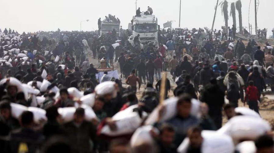 Palestinians carry bags of flour they grabbed from an aid truck near an Israeli checkpoint, as Gaza residents face crisis levels of hunger, amid the ongoing conflict between Israel and Hamas, in Gaza City, February 19, 2024. REUTERS/Kosay Al Nemer/File Photo Purchase Licensing Rights