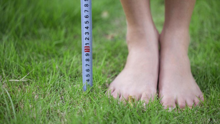 Close-up of person's feet measuring height with measurement tape.
