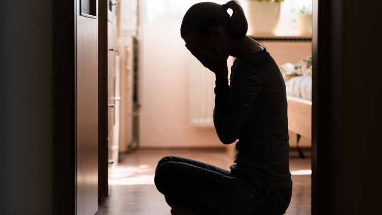 1147847234 Sad young woman sitting on room floor crying with hand over face