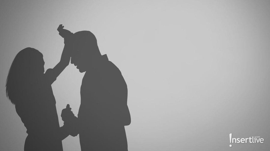 Trying to hide. Abused young woman with her hands in her hair as her abuser stands in front of her