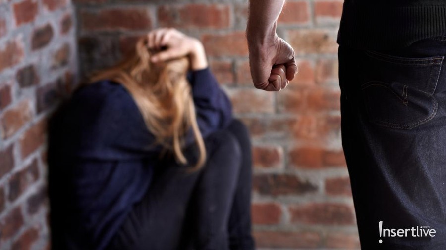 Trying to hide. Abused young woman with her hands in her hair as her abuser stands in front of her