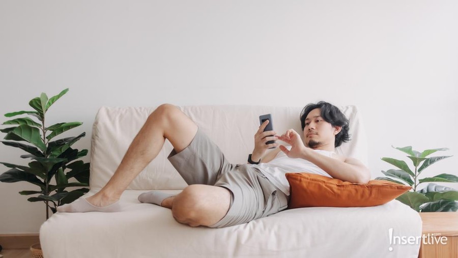 Bored Asian man relaxed and use smartphone for killing time alone in apartment.