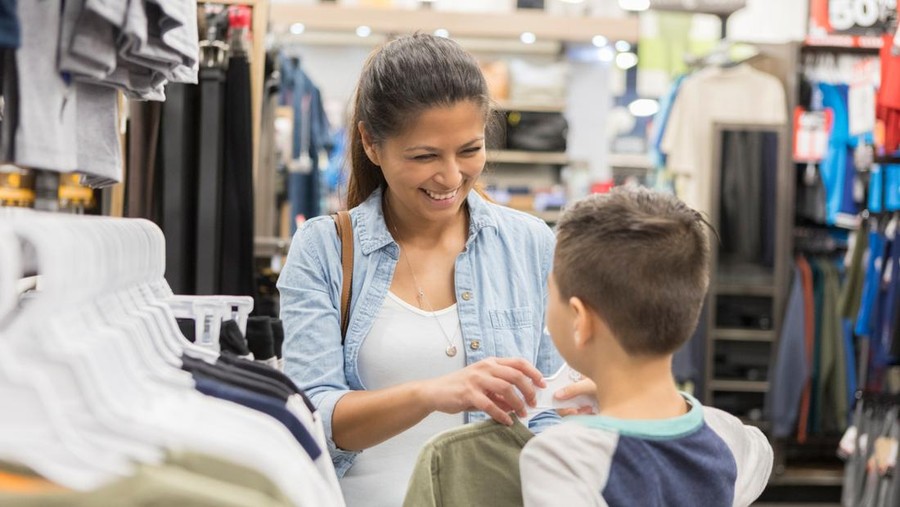 Cheerful mid adult mom picks out clothing for her son. They are shopping in a department store.