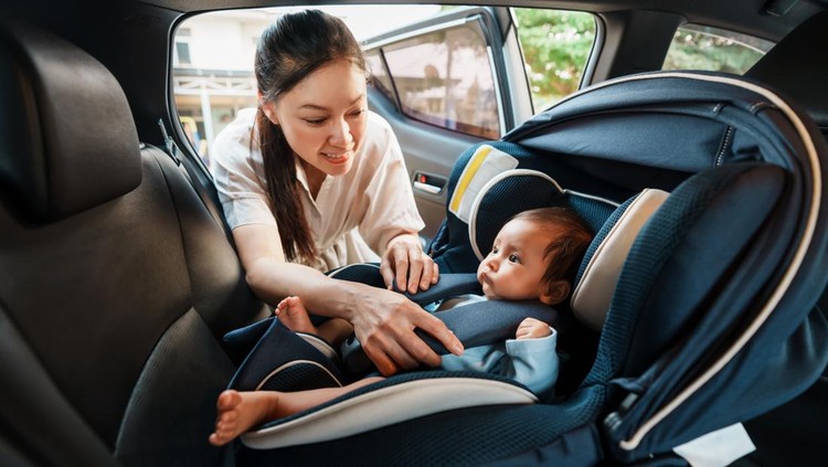 happy mother is fastening safety belt to newborn baby in the car seat