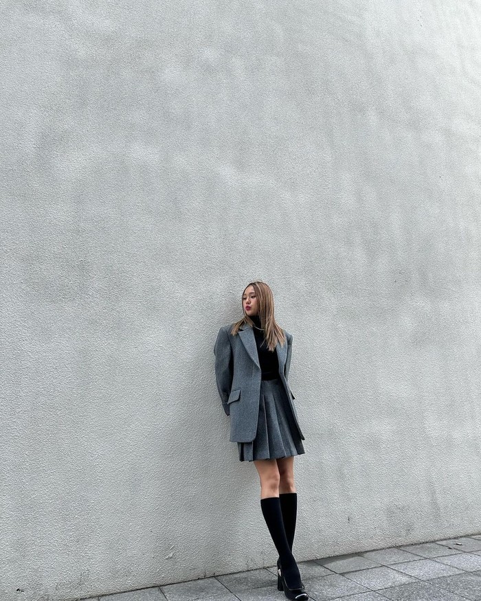 Penampilan Mimi seolah seperti business woman yang elegan. Kesan rapinya dipertegas Mimi dengan mengenakan oversized blazer berwarna abu-abu dan set rok mini lipit. Ia juga mengenakan kaus kaki selutut untuk menonjolkan kesan feminin./ Foto: Elle.co.kr