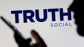 The Truth social network logo is seen displayed behind a woman holding a smartphone in this picture illustration taken February 21, 2022. REUTERS/Dado Ruvic/Illustration/File Photo