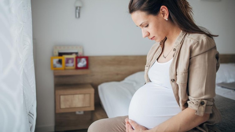 Pregnant young woman grimacing with hands on stomach while sitting at home
