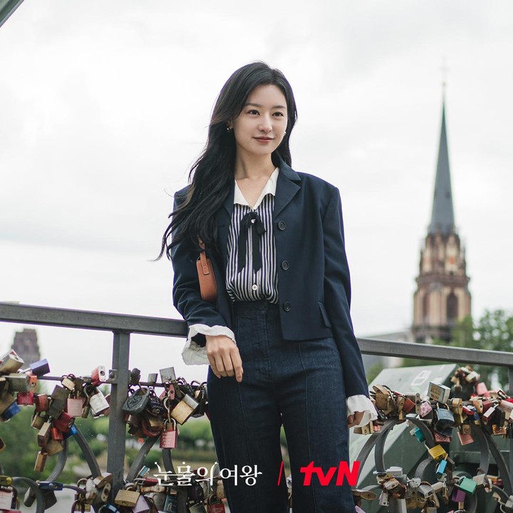 <p>Kemeja stripe biru dan putih dengan pita hitam yang dibalut dalam blazer hitam merupakan outfit Hong Hae In kala ia berkunjung ke Love Lock Bridge. Paduan busana ini cocok untuk dikenakan dalam acara formal dan semi-formal. (Foto: Instagram @tvn_drama)</p>