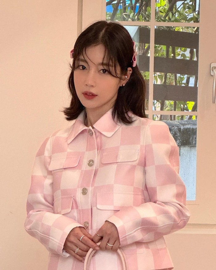 Ki Eun Se memilih jaket baby pink bermotif kotak-kotak dengan tampilan yang energik. Ia melengkapinya dengan jepit rambut pita pink untuk menambahkan sentuhan yang playful dan manis./ Foto: Elle Korea