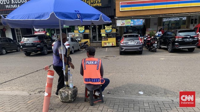 Juru parkir di minimarket kerap dipandang sebelah mata, namun keberadaannya tak jarang dibutuhkan. Mereka bekerja tanpa perlindungan.