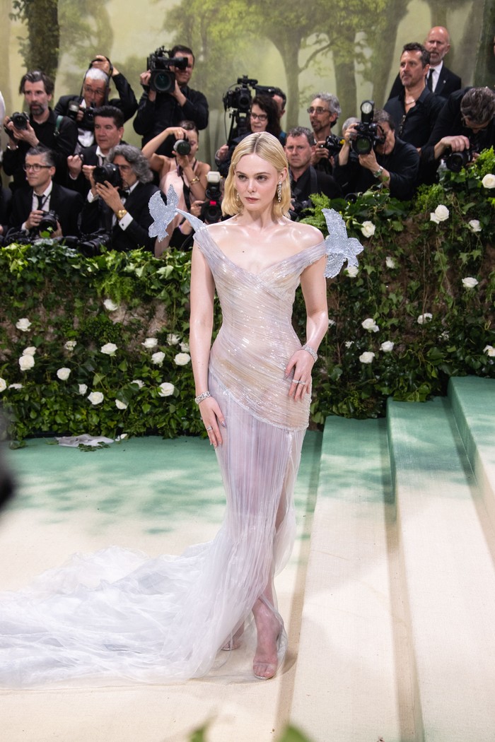 Elle Fanning tampil bak putri dongeng berbalut gaun transparan Balmain. Gaun menyerupai kaca atau pahatan es ini juga dipercantik ornamen burung pada kedua kerah. Perhiasan dari Cartier dan minimalist heels transparan menyempurnakan look-nya./ Foto: Lexie Moreland/WWD via Getty Images