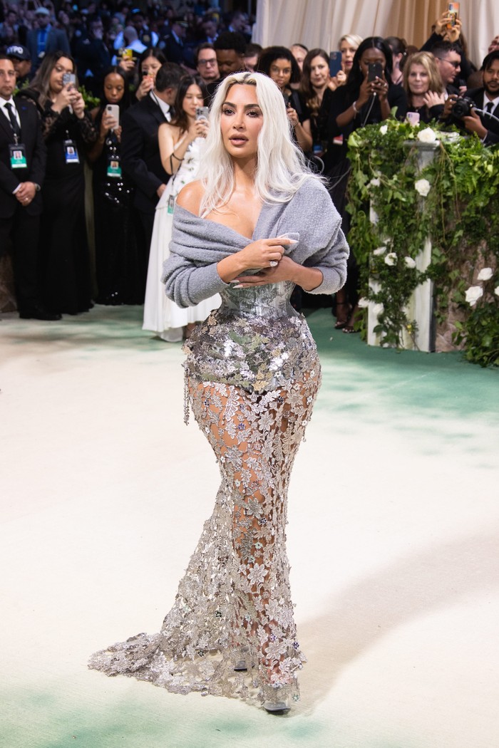 Gaun Maison Margiela kembali dikenakan di green carpet Met Gala 2024. Kim Kardashian memesona dalam dress semi-transparan dengan rok metalik membentuk dedaunan dan bunga saling terkait. Korset ketat rona silver juga di-styling dengan bolero cashmere abu-abu/ Foto: Lexie Moreland/WWD via Getty Images