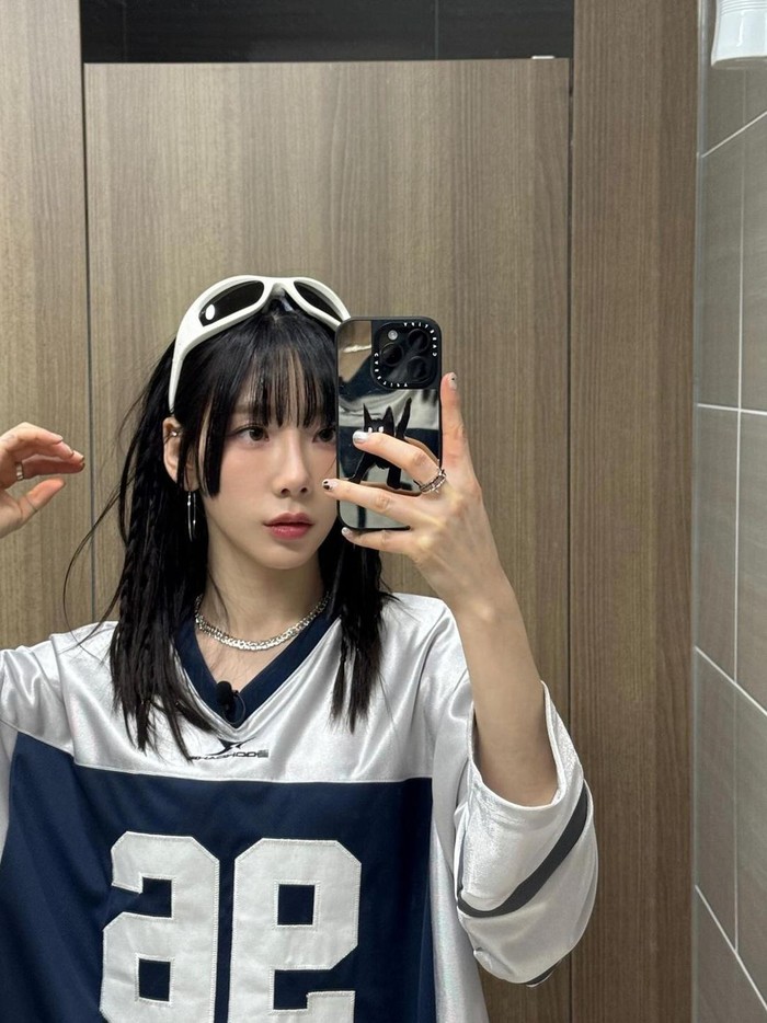 Taeyeon menikmati suasana sporty dengan mengenakan jersey oversize dan kacamata hitam berbingkai unik di atas kepalanya. Ia menambahkan sedikit suasana Y2K dengan menambahkan perhiasan seperti anting bulat dan kalung./ Foto: Elle Korea
