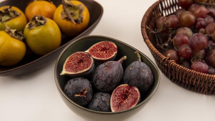 top view of sweet black figs on a bowl with persimmon fruits on a bowl on a white background