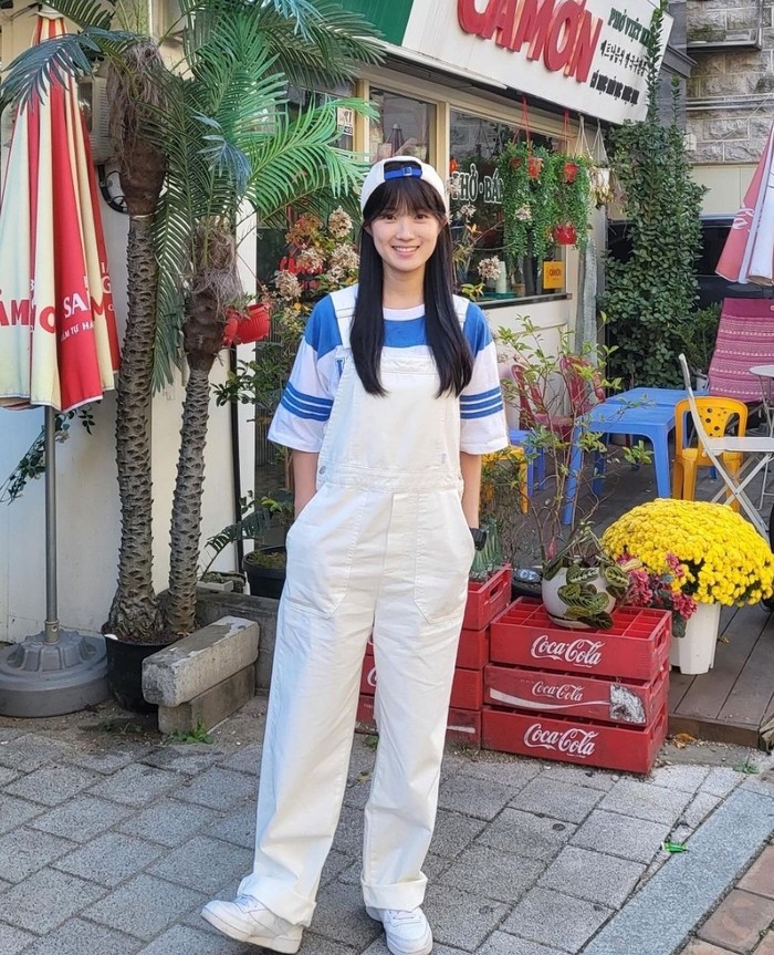 Kim Hye Yoon tampil energik dan cerah dengan jumpsuit overall putih ala awal tahun 2000-an. Ia melengkapi outfitnya dengan kaus oversize garis-garis dan topi yang dihadapkan ke belakang, membuatnya tampil cute dan playful./ Foto: Instagram/hye_yoon1110