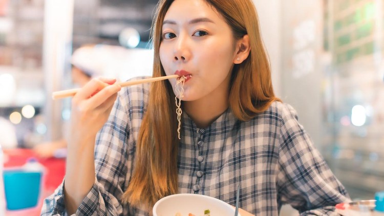 Traveler Asian blogger women travel in Bangkok, Thailand, beautiful female using Women travel in Thailand concept.Woman enjoy her bowl of noodles in outdoor night market in Bangkok city