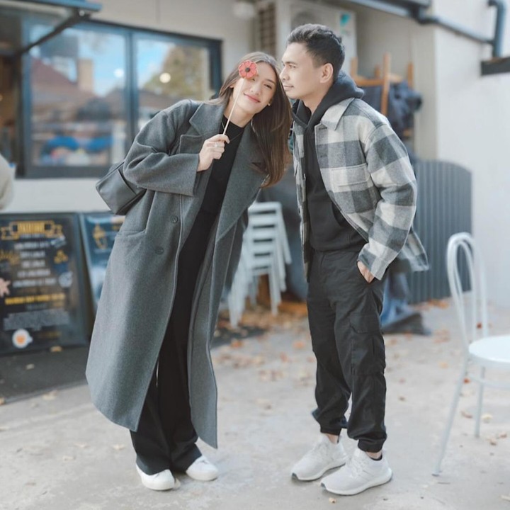 <p>Ketika pergi berlibur, Anissa Aziza dan Raditya Dika pernah mengenakan busana musim gugur bernuansa abu-abu. Anissa memakai<em> trench coat</em> panjang, sedangkan Raditya tampil kasual dengan<em> plaid hoodie</em>. (Foto: Instagram @anissaaziza @raditya_dika)</p>