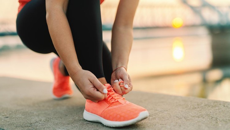 Close up of sporty woman tying shoelace while kneeling outdoor, In background bridge. Fitness outdoors concept.