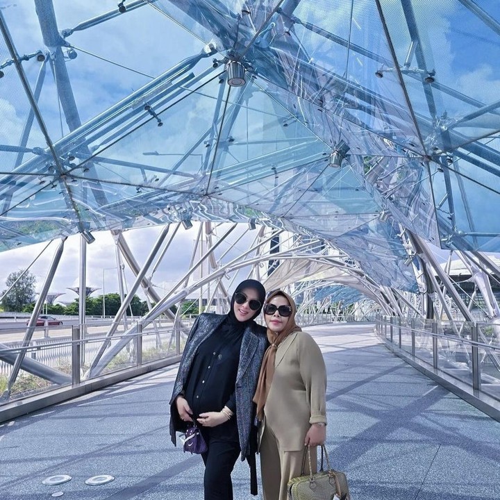 <p>Melalui akun Instagram pribadinya, Syahrini membagikan beberapa potret saat ia sedang asik berfoto dengan sang ibunda di salah satu spot wisata di Singapura. Ibu hamil yang satu ini terlihat berpose di Helix Bridge. (Foto: Instagram @princessyahrini).</p>