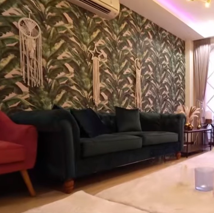 <p>Ketika memasuki rumah, Bunda akan melihat ruang tamu yang cukup luas. Terdapat sofa berwarna merah dan hitam di ruangan ini. Wallpaper ruangan ini didominasi gambar dedaunan hijau. Sementara itu, karpet bulu warna putih terlihat digunakan untuk dekorasi lantai. (Foto: YouTube TRANS7 OFFICIAL)</p>