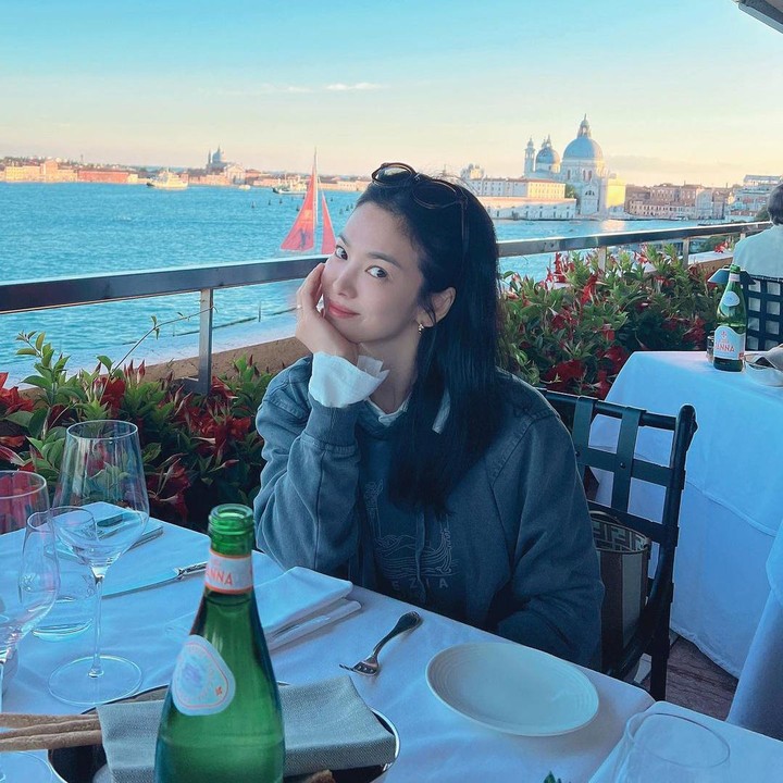 <p>Outfit Song Hye Kyo yang berikutnya bernuansa kasual, memakai kemeja putih yang dibalut dengan sweater berwarna abu-abu ketika menunggu hidangan di sebuah restoran. (Foto: Instagram @kyo1122)</p>