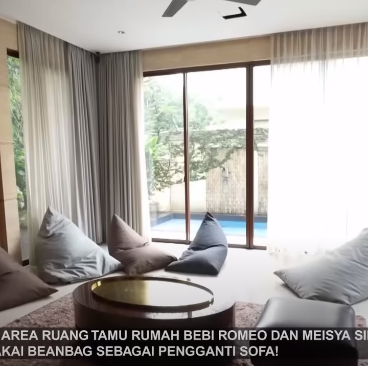 <p>Masuk ke dalam rumah, Bunda akan melihat ruang tamu yang cukup luas. Berbeda dengan kebanyakan rumah, ruang tamu Meisya dan Bebi tidak menggunakan sofa untuk tamu duduk. Pasangan ini meletakkan beberapa bean bag di lantai untuk duduk. Tampak pula hiasan dinding dari batu onyx senilai puluhan juta rupiah. (Foto: YouTube TRANS7 OFFICIAL)</p>