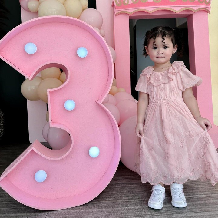 <p>Aiko terlihat memesona mengenakan dress warna merah muda dan rambut yang keriting. Dekorasi pesta pun terlihat cantik dengan angka tiga yang besar dan balon warna merah muda serta kuning. (Foto: Instagram: @revtiayunatasya)</p>