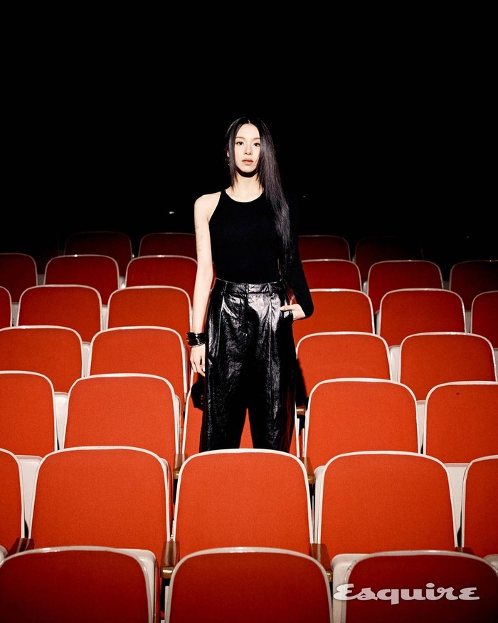 Pada konsep foto photobook kedua, aura Chaeyoung semakin bersinar dengan berdiri percaya diri dalam ruangan gelap dipenuhi kursi merah yang sorot cahayanya hanya menyorot kearahnya./ Foto: instagram.com/esquire.korea