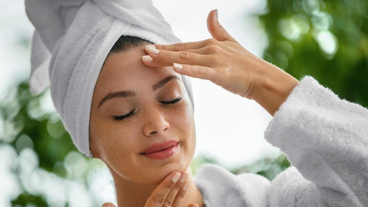 Young woman massaging face with her eyes closed. She's in the bathrobe and her hair is wrapped in the towel.