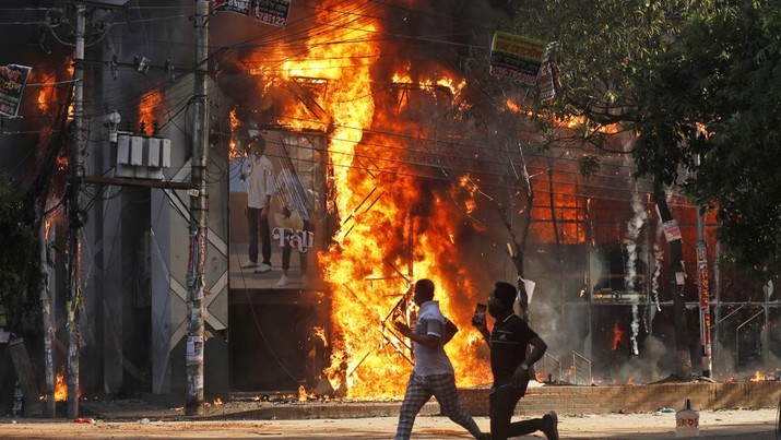 Pria berlari melewati pusat perbelanjaan yang dibakar oleh pengunjuk rasa selama unjuk rasa menentang Perdana Menteri Sheikh Hasina dan pemerintahannya yang menuntut keadilan bagi para korban yang tewas dalam bentrokan mematikan baru-baru ini di seluruh negeri, di Dhaka, Bangladesh, Minggu, 4 Agustus 2024. (AP Photo/Rajib Dhar)