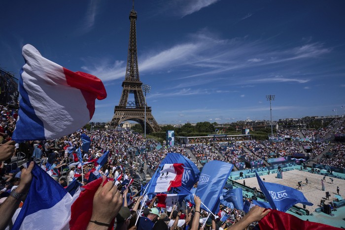 Supporters for France wave flags during the women's pool C beach volleyball match between Germany and France at Eiffel Tower Stadium, at the 2024 Summer Olympics, Sunday, July 28, 2024, in Paris, France. (AP Photo/Louise Delmotte)