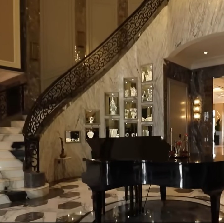 <p>Ketika memasuki rumah, ada area <em>foyer</em> yang dibuat bak <em>lobby</em> hotel dengan dua tangga melingkar di sisi kanan dan kiri. Di tengahnya, terdapat piano dan pajangan kristal yang tersimpan di lemari dinding. (Foto: YouTube TRANS7 OFFICIAL)</p>