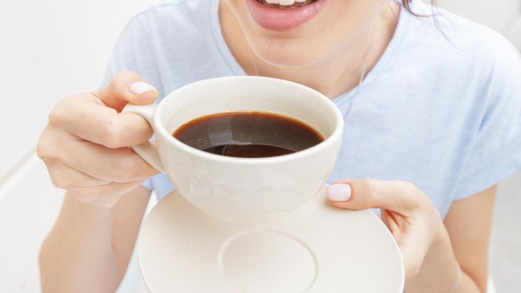 Happy woman drinks a black espresso coffee and smiles&period; The concept of problems with the color of teeth from bad habits