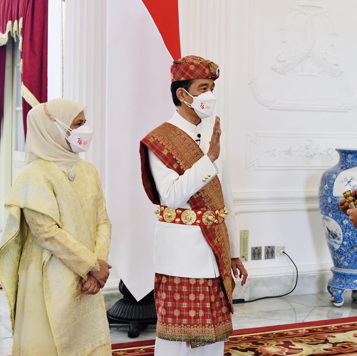 <p>Pada 2021, Presiden Jokowi masih menghadiri upacara HUT RI di tengah suasana pandemi COVID-19. Kala itu, ia memakai pakaian adat Pepadun dari Provinsi Lampung yang terdiri dari baju lengan panjang putih dan dipadukan dengan celana panjang berwarna senada. Ia juga memakai sarung tumpal khas Lampung untuk menutupi bagian celana. Penampilannya disempurnakan dengan kain selendang, ikat pinggang, dan tutup kepala bernuansa merah. Sementara itu, Iriana tampil anggun dengan busana nasional dan hijab berwarna gading lengkap dengan kain songket. (Foto: BPMI Setpres/Laily RE)</p>