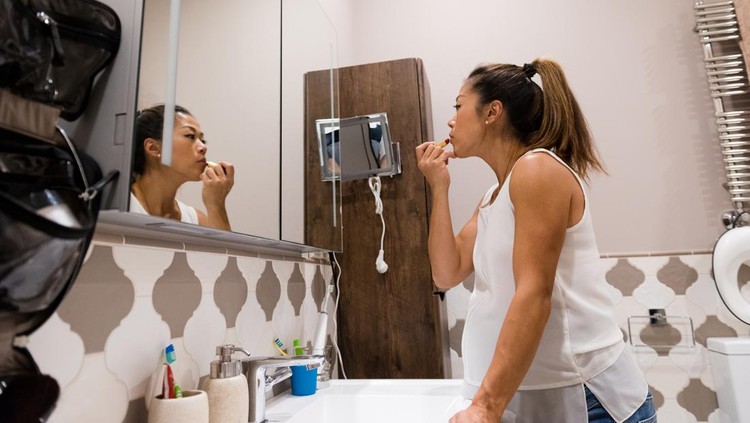 Confident pregnant woman gets dressed for the day. She is looking in the bathroom mirror while applying lipstick.
