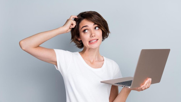 Portrait of puzzled woman wear stylish t-shirt hold laptop finger scratching head look empty space isolated on gray color background.