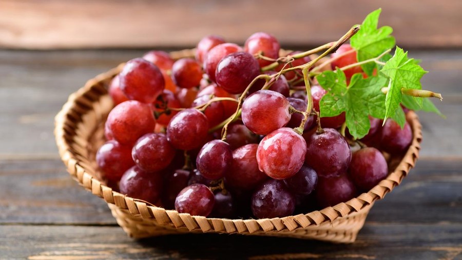 Fresh red grapes fruit in a basket on wooden background