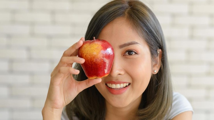 Portrait of smiling beautiful young asian woman holding red apple. close up