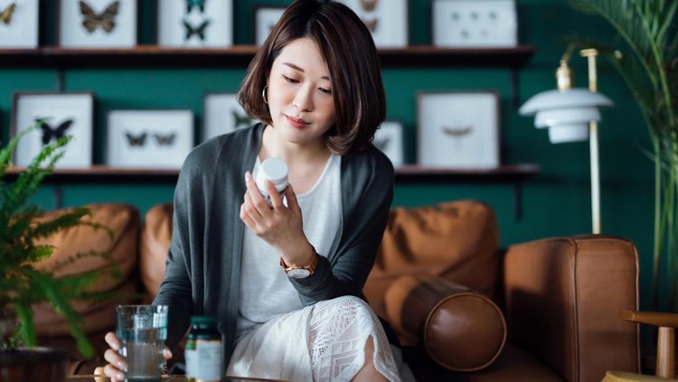 High angle view, Asian teenage woman pours medicine into her hand while sitting on a sofa in the living room. Healthcare and medicine concept