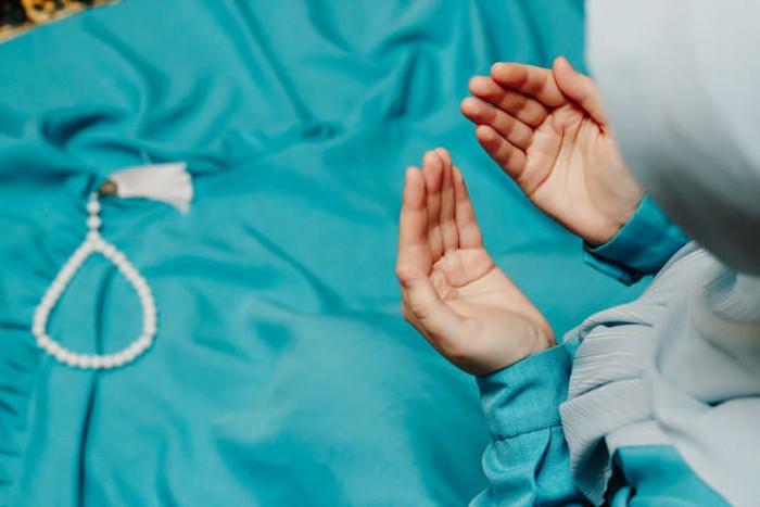 Muslim woman in a headscarf praying and a prayer beads in the background