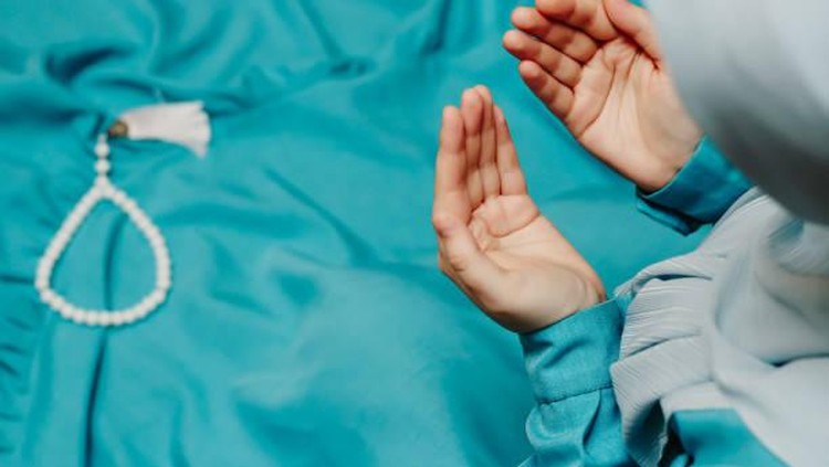 Ilustrasi berdoa sebelum tidur. Muslim woman in a headscarf praying and a prayer beads in the background