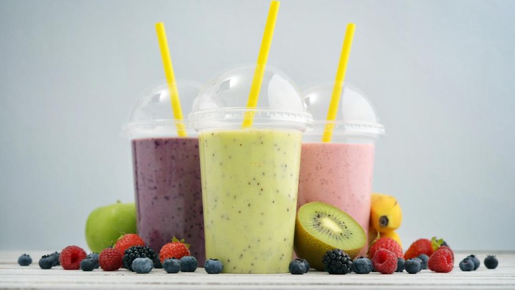Fruit smoothies in plastic cups with blueberry, strawberry, kiwi, blackberry, raspberry and banana on blue background. Take away drinks concept.