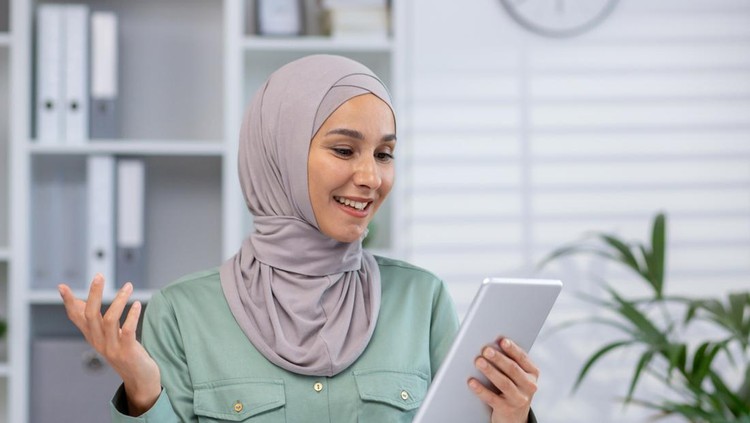 Ilustrasi wanita hijab pidato islami Smiling woman wearing hijab, using tablet in modern office with bookshelf and plants in the background.