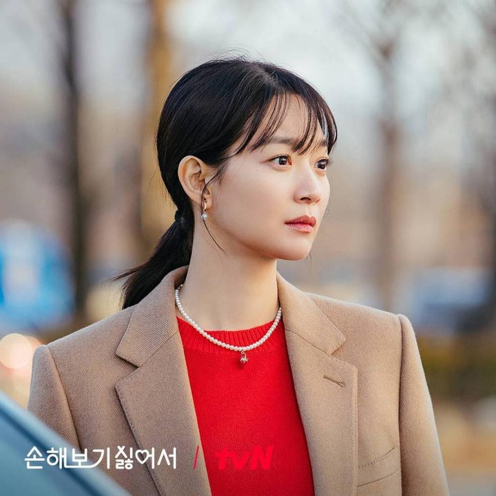 <p>Shin Min Ah memberi sentuhan warna cerah pada <em>blazer</em> cokelat polosnya. Ia mengenakan <em>inner</em> berwarna merah cerah, lengkap dengan kalung yang mencuri perhatian. (Foto: Dok. tvN)</p>
