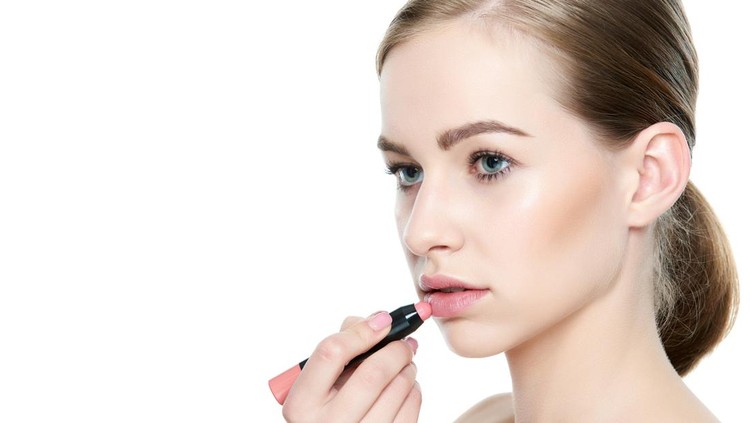 Beautiful young blond woman  applying coral color lipstick. Beauty portrait isolated over white background with copy space.